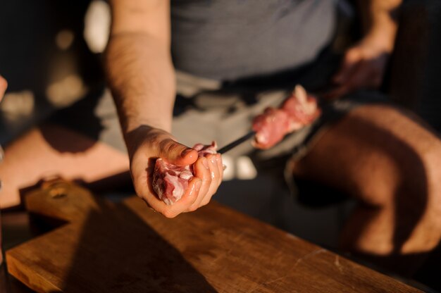 Sitzender Mann, der Stücke Frischfleisch auf Stahlaufsteckspindeln aufreiht