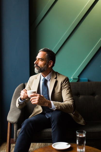 Sitzender und trinkender Kaffee des hübschen reifen Mannes