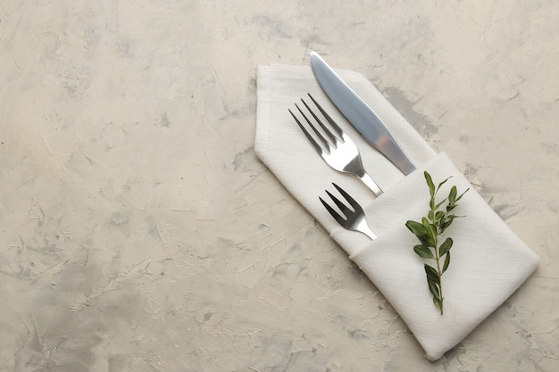 Sitzordnung bei Tisch. Besteck. Gabel, Messer in einer weißen Serviette auf einem hellen Betontisch. Ansicht von oben