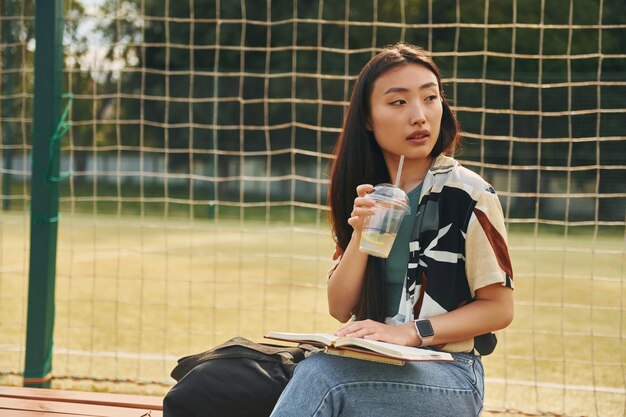 Sitzt gegen Sportplatz Junge asiatische Frau ist tagsüber im Freien
