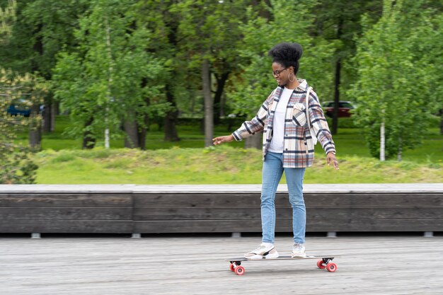 Skate e estilo de vida urbano moderno casual jovem africana em longboard no parque da cidade