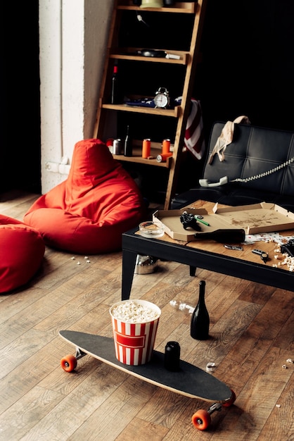 Skateboard mit Popcorn-Box neben Couchtisch im unordentlichen Wohnzimmer