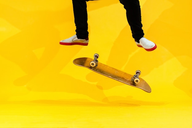 Foto skateboarder, der skateboard-trick durchführt - kick-flip im studio. sportler üben stunt-sprung auf gelbem hintergrund und bereiten sich auf den wettbewerb vor. extremsport, jugendkultur