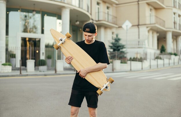 Skateboarder mit Longboard steht auf Architekturhintergrund auf der Straße