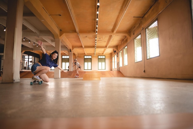 Skater-Frau, die Skateboard in der Sporthalle spielt. Junge asiatische Frau ist glücklich und macht Spaß mit dem Skateboard-Lebensstil in der trendigen Mode der Teenager-Hipster-Frauen in der Stadt