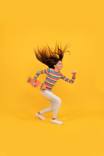 Skater niño enérgico en ropa colorida. patineta de centavo. andar en patineta. niño feliz salta con tablero de centavo. chica adolescente sobre fondo amarillo. ser un hipster. actividad infantil.