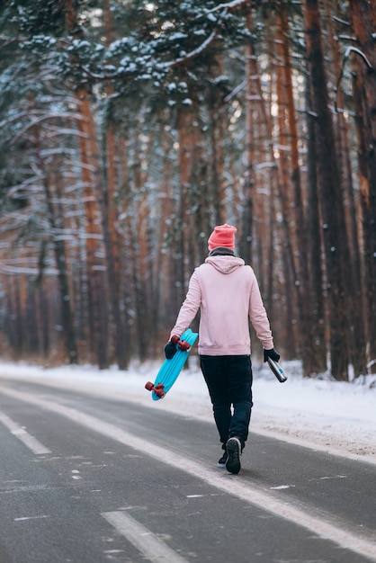 Skater de pie en la carretera en medio del bosque rodeado de nieve