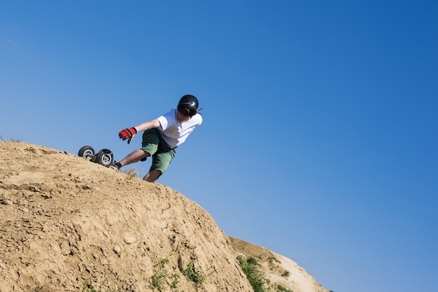 Skater saltando con mountainboard sobre la colina con cielo azul