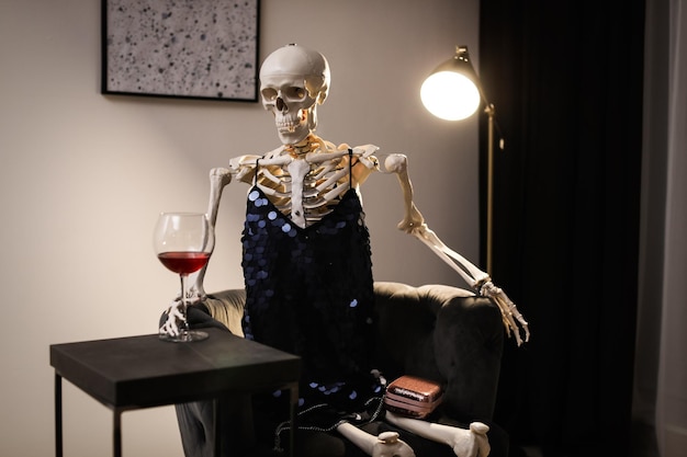 Skelett im Kleid mit Wein drinnen am Tisch sitzen