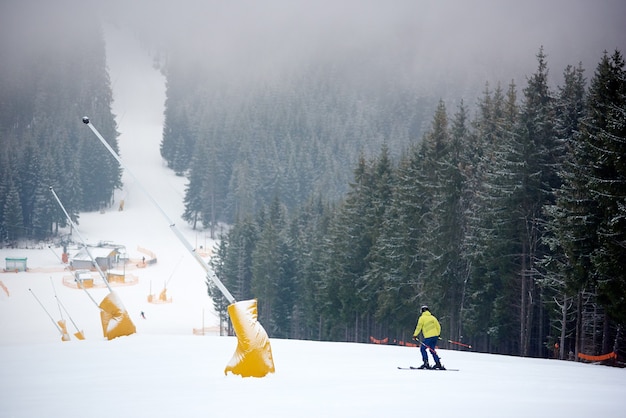 Skifahrer beim Freeriden im Schneefall am Berghang mit Sessellift im dichten Nadelwald. Rückansicht