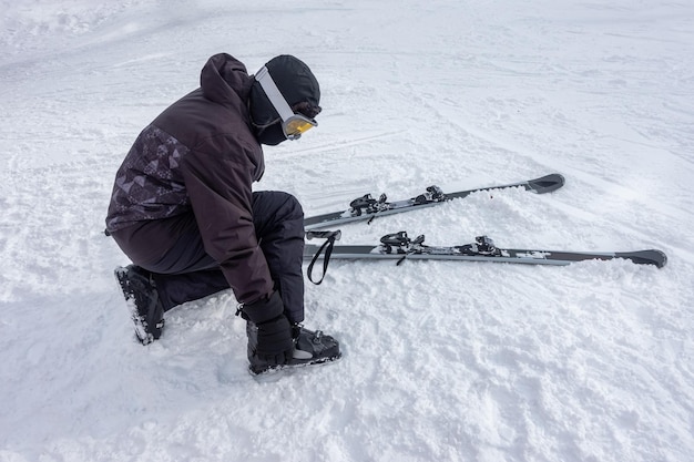 Skifahrer bereitet sich auf das Skifahren vor, indem er Stiefel an den Füßen anbringt und die Ausrüstung überprüft