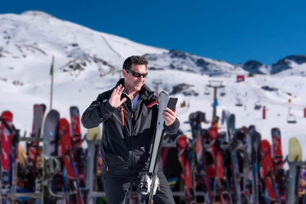 Skifahrer, der einen Videoanruf vom Skigebiet mit dem schneebedeckten Berg im Hintergrund tätigt