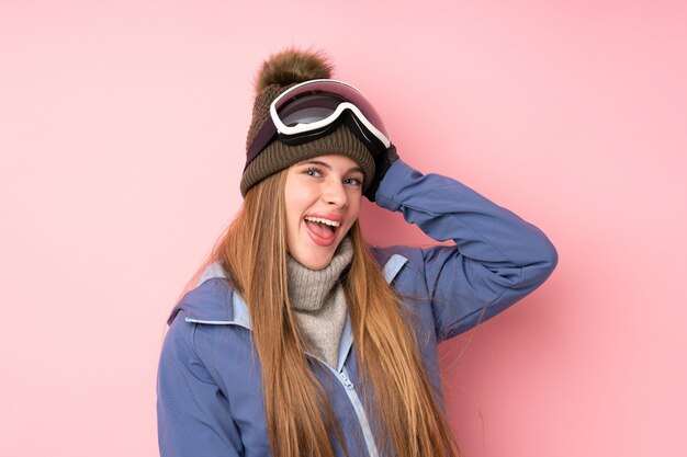 Skifahrerjugendlichmädchen mit snowboardinggläsern über getrenntem rosafarbenem lachen