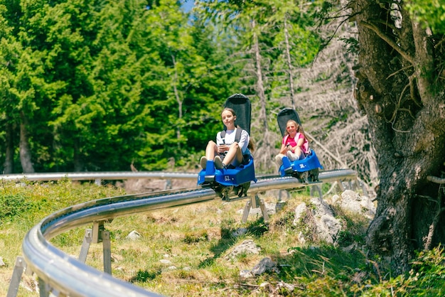 Skigebiet Mountain Coaster Zwei Mädchen gehen hintereinander die Skipiste hinunter Wald und Bäume im Hintergrund