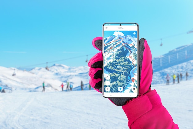 Skikarte auf dem Smartphone in der Hand der Frau mit rosafarbenem Handschuh Ski- und Snowboard-App-Konzept für das Routen- und Entfernungsverfolgungskonzept Skifahrer und Skipisten im Hintergrund