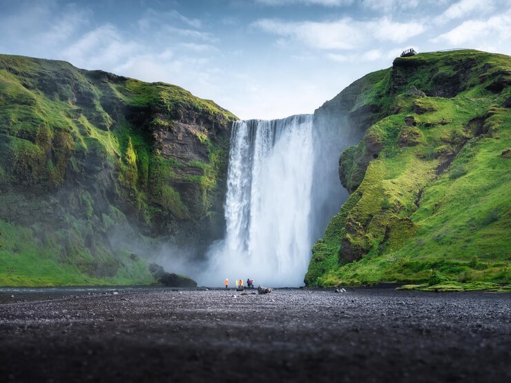 Skogafoss-Wasserfall Island Bergtal und klarer Himmel Naturlandschaft in der Sommersaison Isländische Natur Gruppe von Menschen in der Nähe eines großen Wasserfalls Reisebild