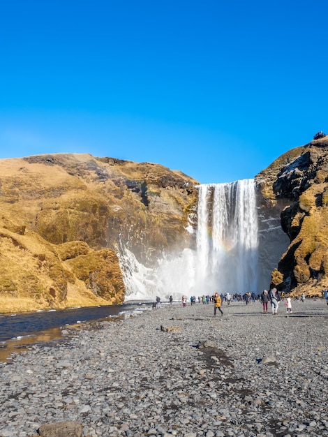 Skogafoss-Wasserfall mit Regenbogenbrechung mit schnee- und eisüberfüllten Touristen in Island