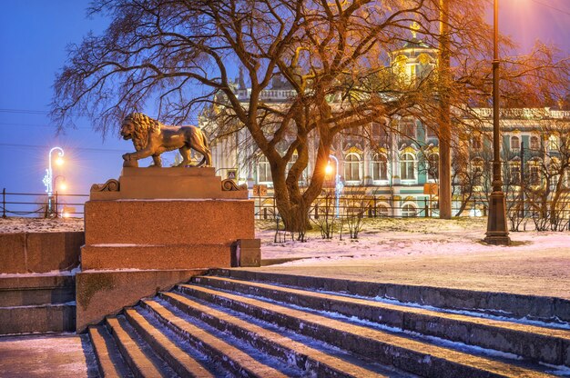 Skulptur eines Löwen auf dem Newa-Damm in St. Petersburg und der Eremitage durch die Zweige an einem Wintermorgen