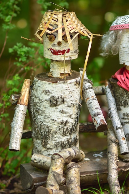 Skulptur eines Mannes aus Baumstämmen, auf dem ein hölzerner Mann mit Hut sitzt