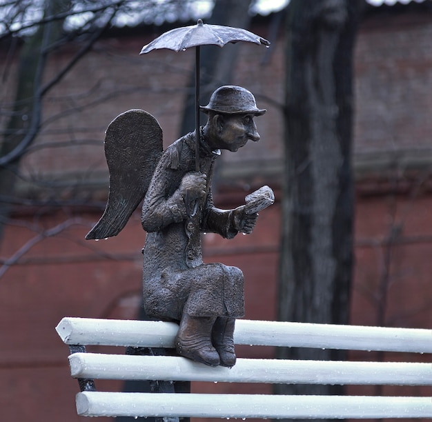 Skulptur eines Sankt Petersburg Engels unter einem Regenschirm mit einem Buch auf einer weißen Bank in Sankt Petersburg
