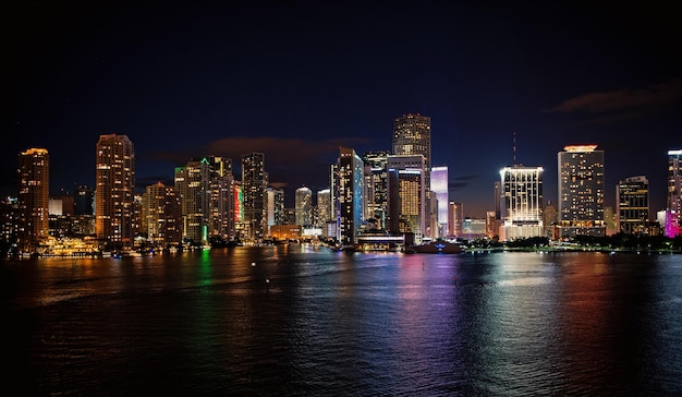 Skyline-Panorama von Miami City mit städtischen Wolkenkratzern mit heller Beleuchtung auf dunklem Meerwasser am Nachthimmel in Miami, USA. Architektur, Bau, Wahrzeichen, Reisekonzept