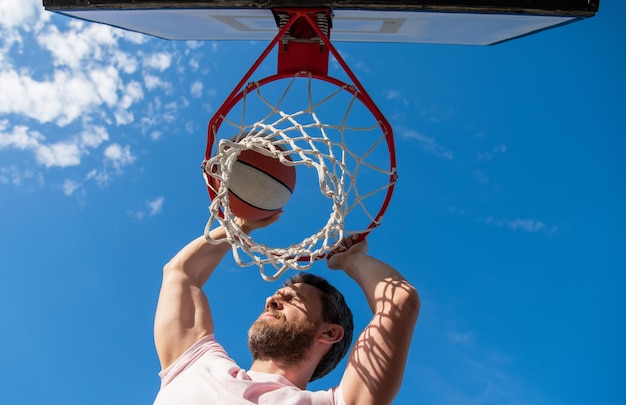 Slam dunk em movimento atividade de verão pulando homem com bola de basquete na quadra profissional jogador de basquete treinando cara ao ar livre tem esporte motivação esporte e hobby enterrada na cesta