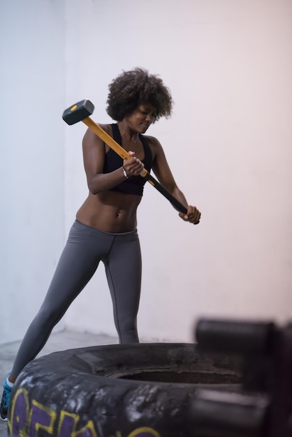 Sledgehammer Tire Hits afroamerikanische Frau trainiert im Fitnessstudio mit Hammer und Traktorreifen