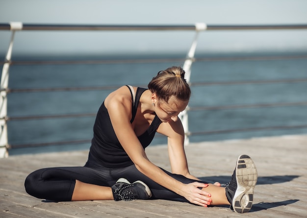 Slim fit mujer en ropa deportiva haciendo estiramientos de piernas en la playa en un día soleado