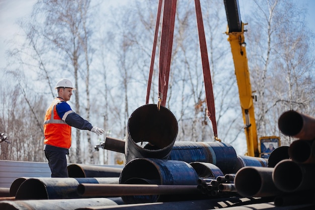 Slinger im Helm entlädt Metallrohre auf der Baustelle an einem sonnigen Sommertag Echte Szene Echter Arbeiter