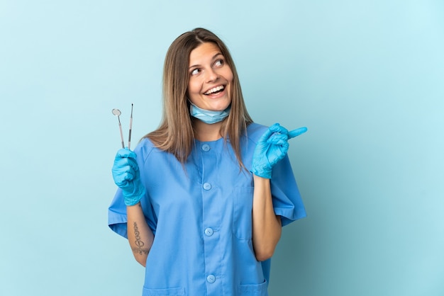 Slowakischer Zahnarzt, der auf blauem Hintergrund isolierte Werkzeuge hält, die die Lösung realisieren möchten, während er einen Finger hochhebt