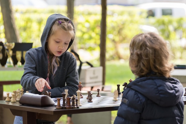 Smart Girl de sete anos está participando de um torneio de xadrez infantil ao ar livre no parque