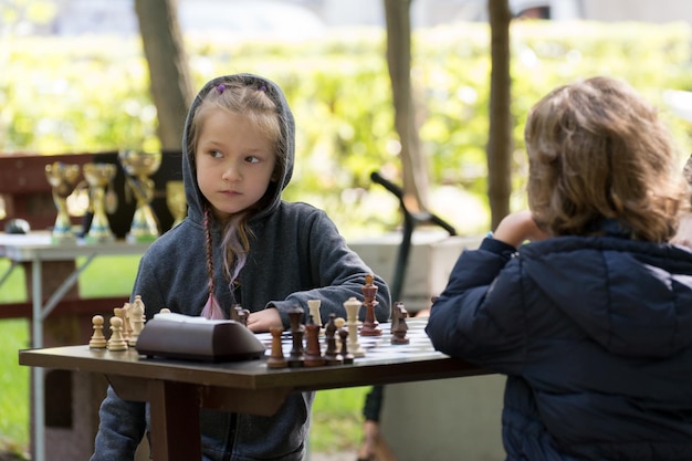 Smart Girl de sete anos está participando de um torneio de xadrez infantil ao ar livre no parque