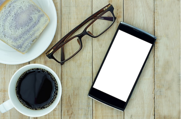 Smartphone, anteojos y una taza de café con pan sobre fondo de madera