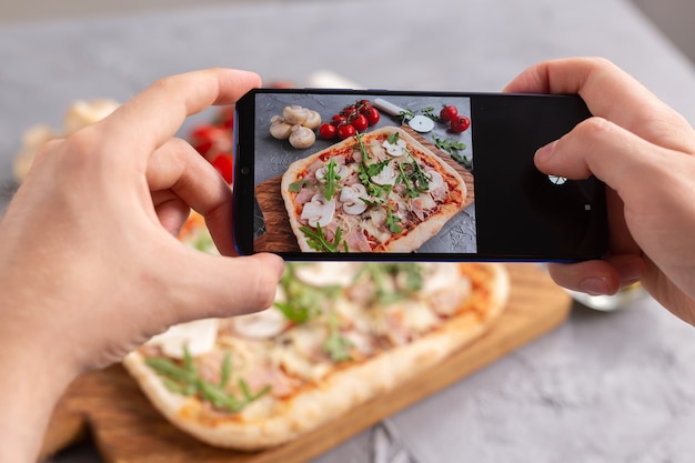 Smartphone atirou em comida. pizza tradicional italiana com queijo, fiambre e cogumelos. redes sociais e conceito de aplicativo de entrega de comida.