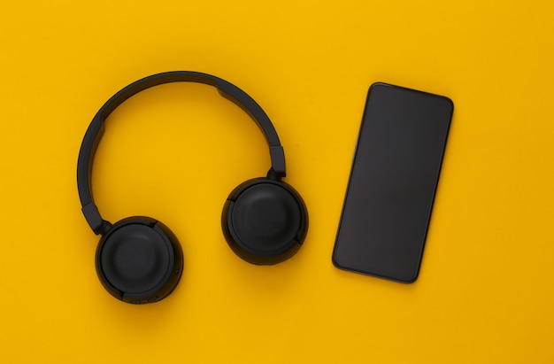 Smartphone con auriculares estéreo negros sobre un amarillo