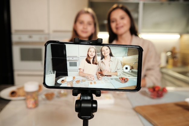 Smartphone-Bildschirm während des Livestreams der Meisterklasse der Hausmannskost, in der zwei junge Frauen hausgemachtes Eis in der Küche zubereiten