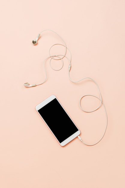 Smartphone blanco con auriculares blancos en una mesa en colores pastel