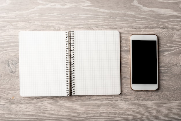 Foto smartphone blanco con un cuaderno sobre una mesa de madera