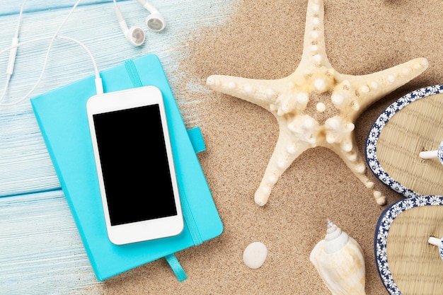 Smartphone y bloc de notas en madera con estrellas de mar y conchas.