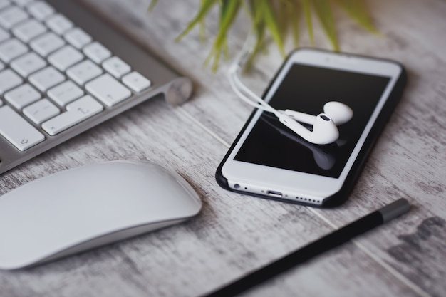 Smartphone branco com fones de ouvido e teclado na mesa