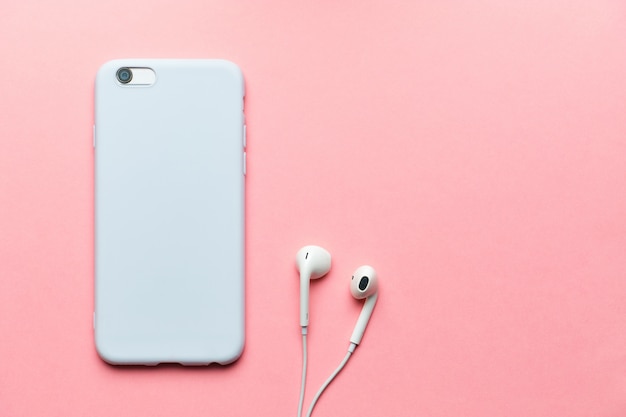 Smartphone branco com fones de ouvido em um fundo rosa