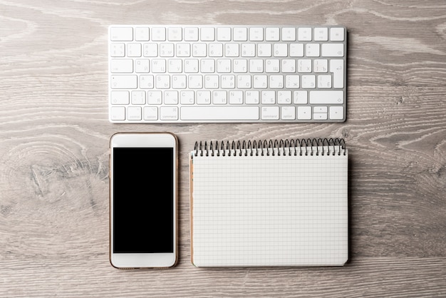 Smartphone branco com um notebook em uma mesa de madeira