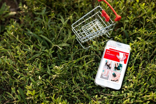 Smartphone y carrito de compras sobre la hierba verde. Compras en línea o concepto de comercio electrónico en el sitio web para el medio ambiente.