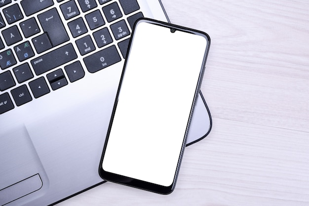 Smartphone, celular com tela branca em um laptop cinza na área de trabalho.