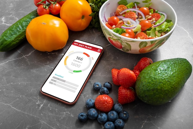 Smartphone com aplicativo de planejamento de refeições saudáveis em um balcão de cozinha cercado por legumes e frutas