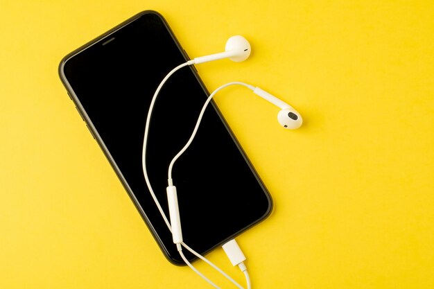 Smartphone com fones de ouvido em fundo amarelo A vista de cima Ouça música