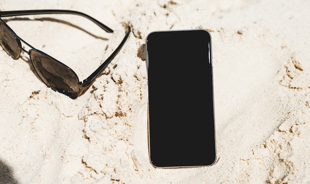 Smartphone com tela em branco na praia com óculos de sol