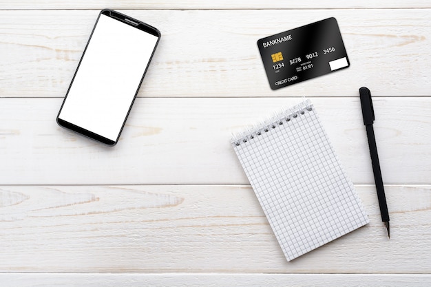 Smartphone, cuaderno, bolígrafo y tarjeta de crédito en una mesa blanca