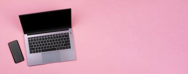 smartphone e uma maquete preta na tela de um laptop em uma vista superior de fundo rosa