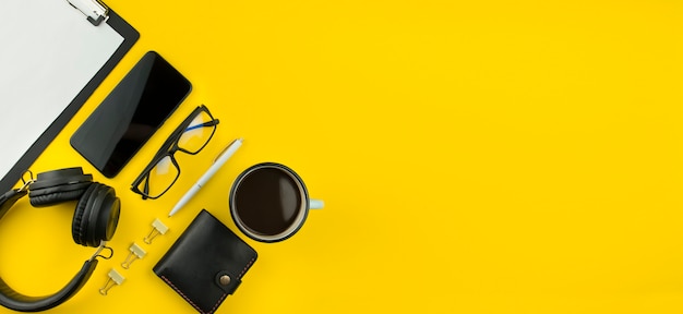 Smartphone, fones de ouvido e acessórios de escritório em um fundo amarelo. Estilo de vida moderno. O negócio. Postura plana. Bandeira. Copie o espaço.